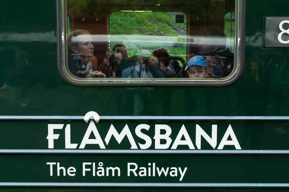 Passengers looking through the window of a green Flåm Railway train in Norway.
