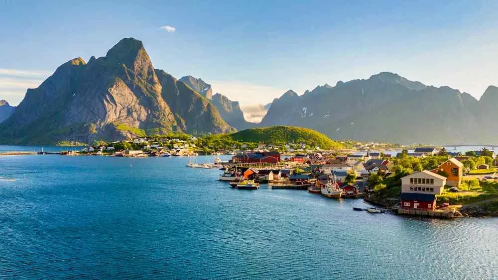 Panoramic view of a coastal village in the Lofoten Islands surrounded by blue water and dramatic rugged mountains.