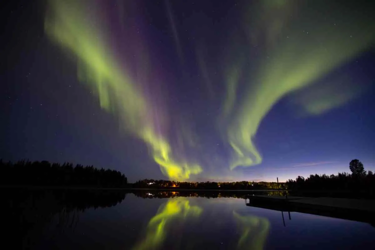 Vue d'ensemble d'une aurore boréale aux teintes jaunâtres au-dessus d'un lac calme, la nuit.