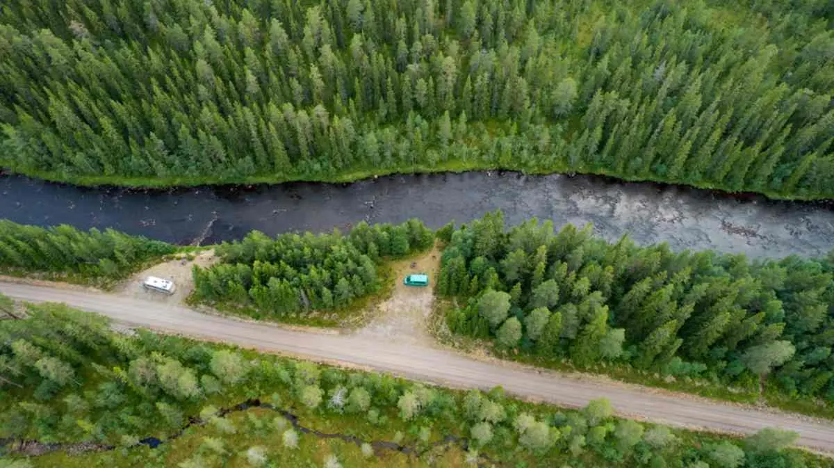 Vue aérienne prise par drone de plusieurs véhicules garés dans une forêt près d'un lac.