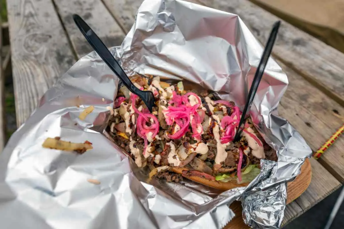Gros plan sur un pain plat de type kebab garni de viande grillée, d’oignons marinés et de sauce, présenté sur du papier d’aluminium.
