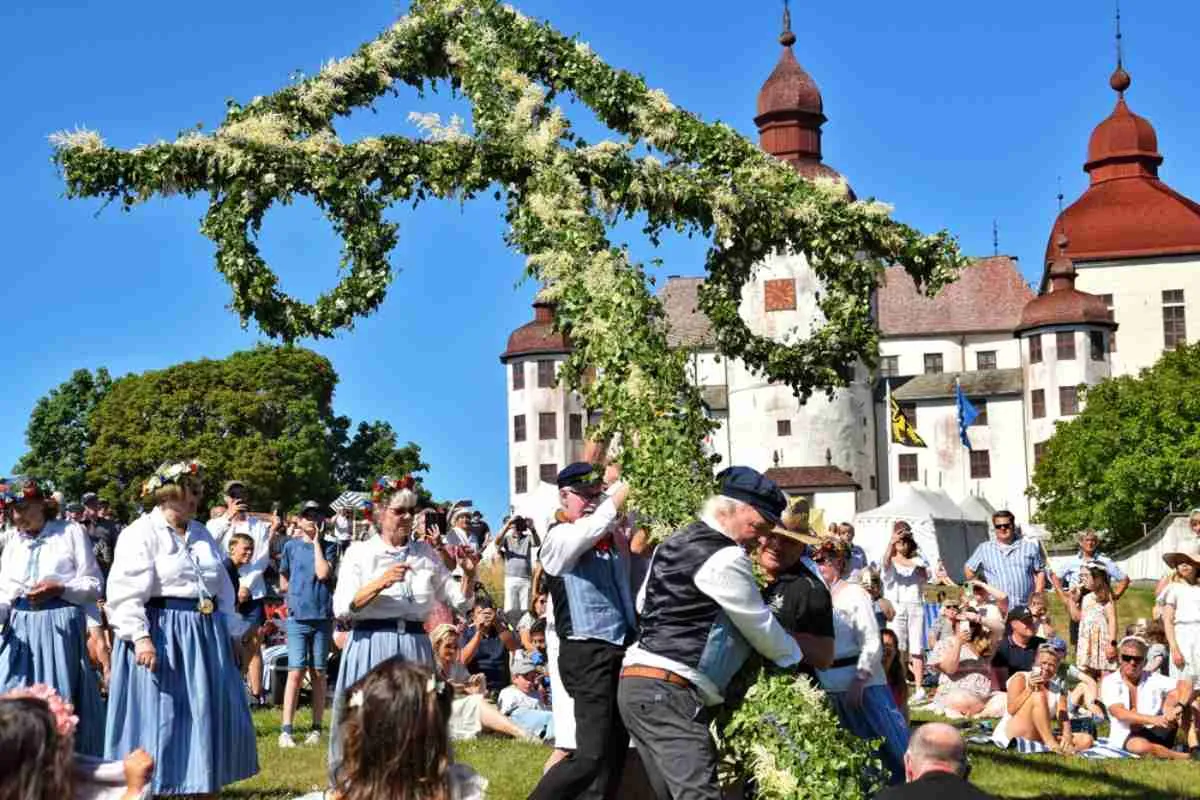 Un grupo de personas vestidas con ropa típica sueca levanta una cruz de flores para celebrar la llegada del verano.