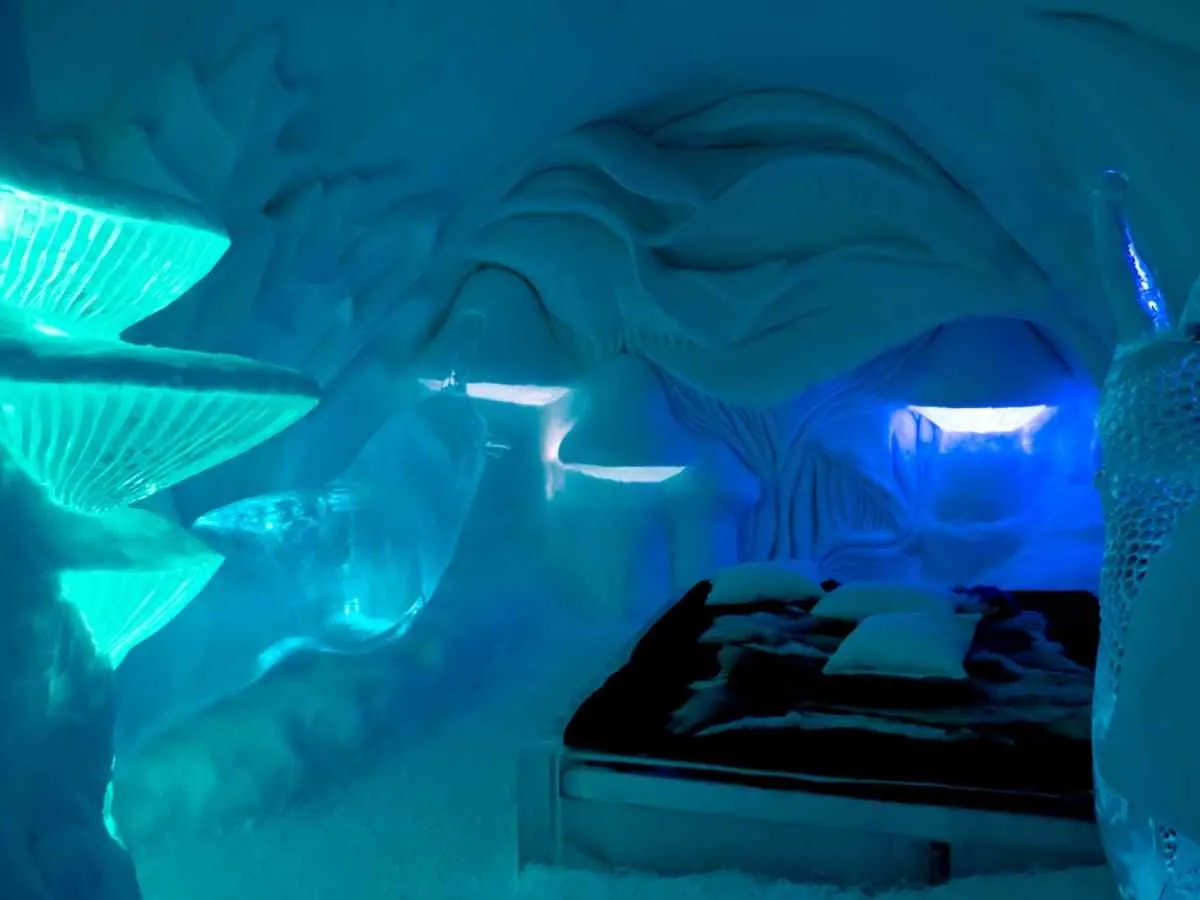 Vista del interior de uno de los dormitorios del famoso Icehotel de Suecia, completamente recubierto de hielo e iluminado con luces que parecen recrear la aurora boreal de la zona, con una cama negra.