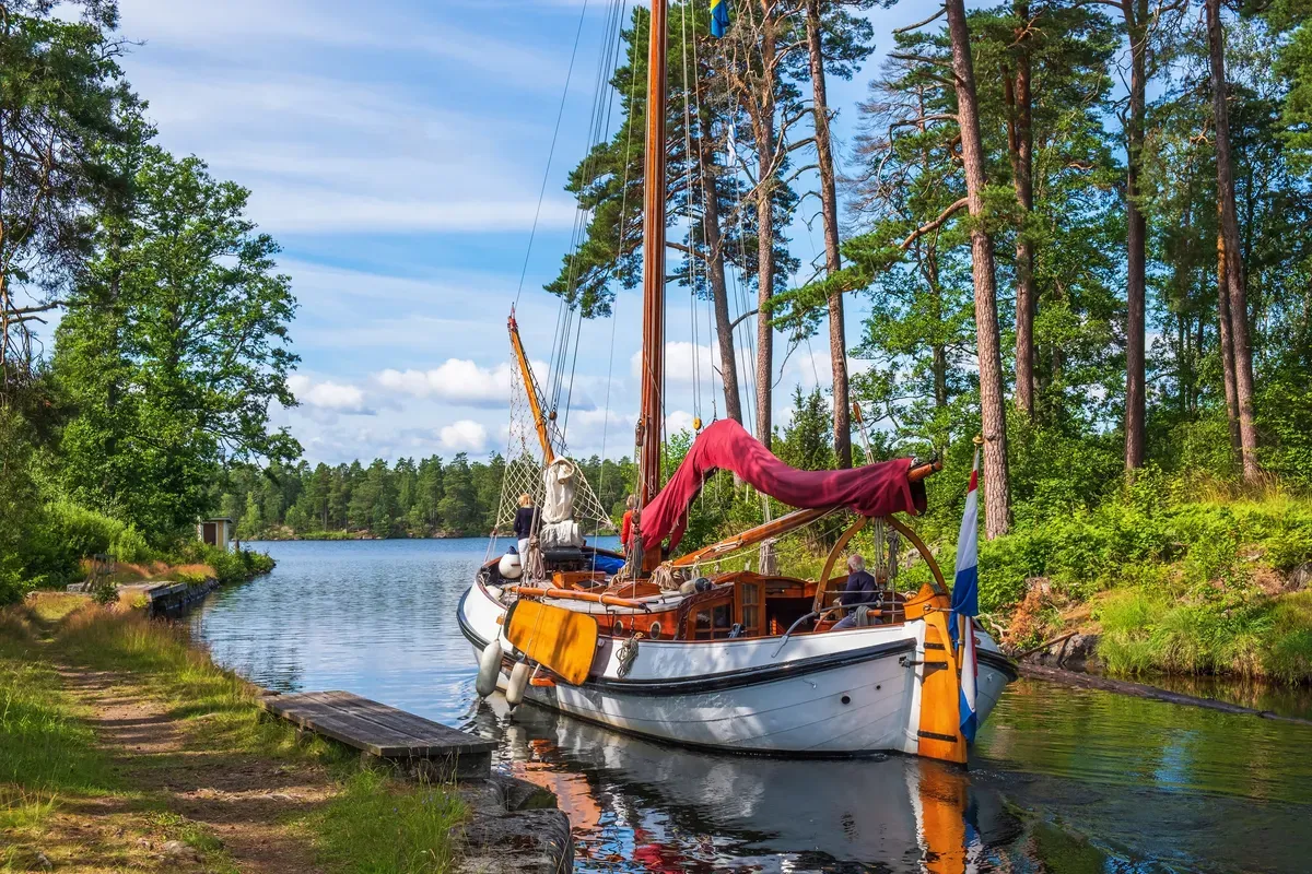 Un velero tradicional de madera amarrado en un tramo estrecho y boscoso del canal de Göta en un tranquilo día de verano.
