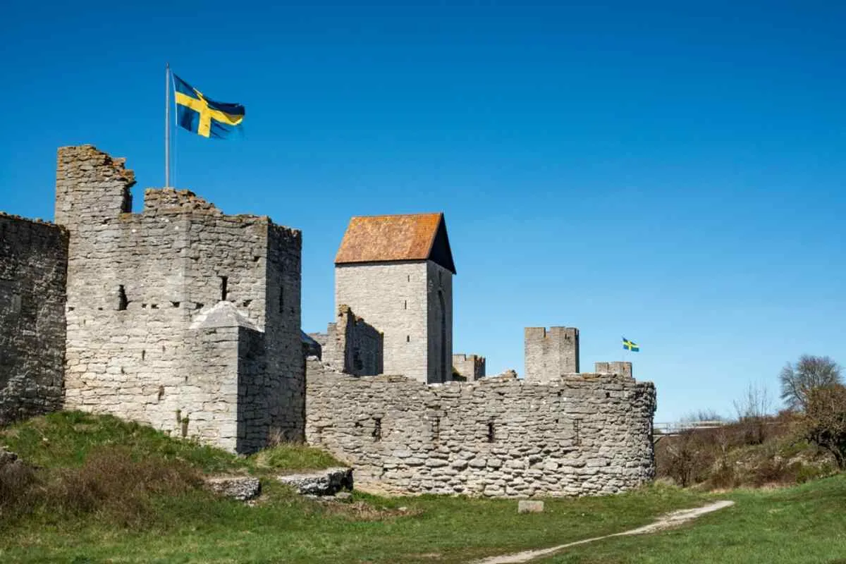 Les anciens remparts médiévaux en pierre de Visby, sur l'île de Gotland, en Suède, avec le drapeau suédois flottant sous un ciel bleu limpide.