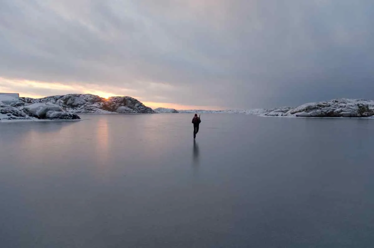 Vista general de un lago helado en el que se ve a una persona patinando sobre él.