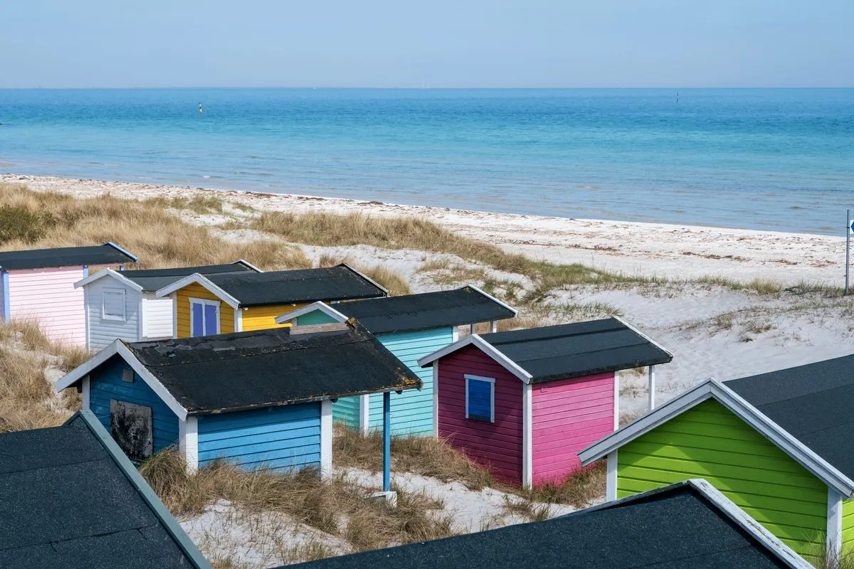 Vista dal drone delle case colorate che fanno da contrasto con la sabbia bianca della spiaggia svedese sulla costa di Skane.