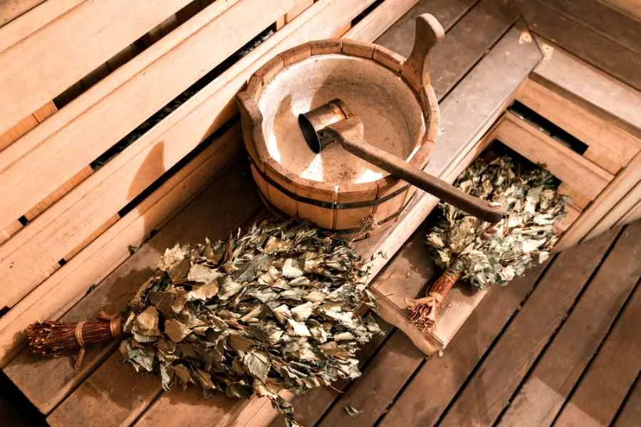Schema dettagliato degli strumenti e delle piante utilizzati nella sauna svedese per il riscaldamento e la purificazione, riportato su una tavola di legno.