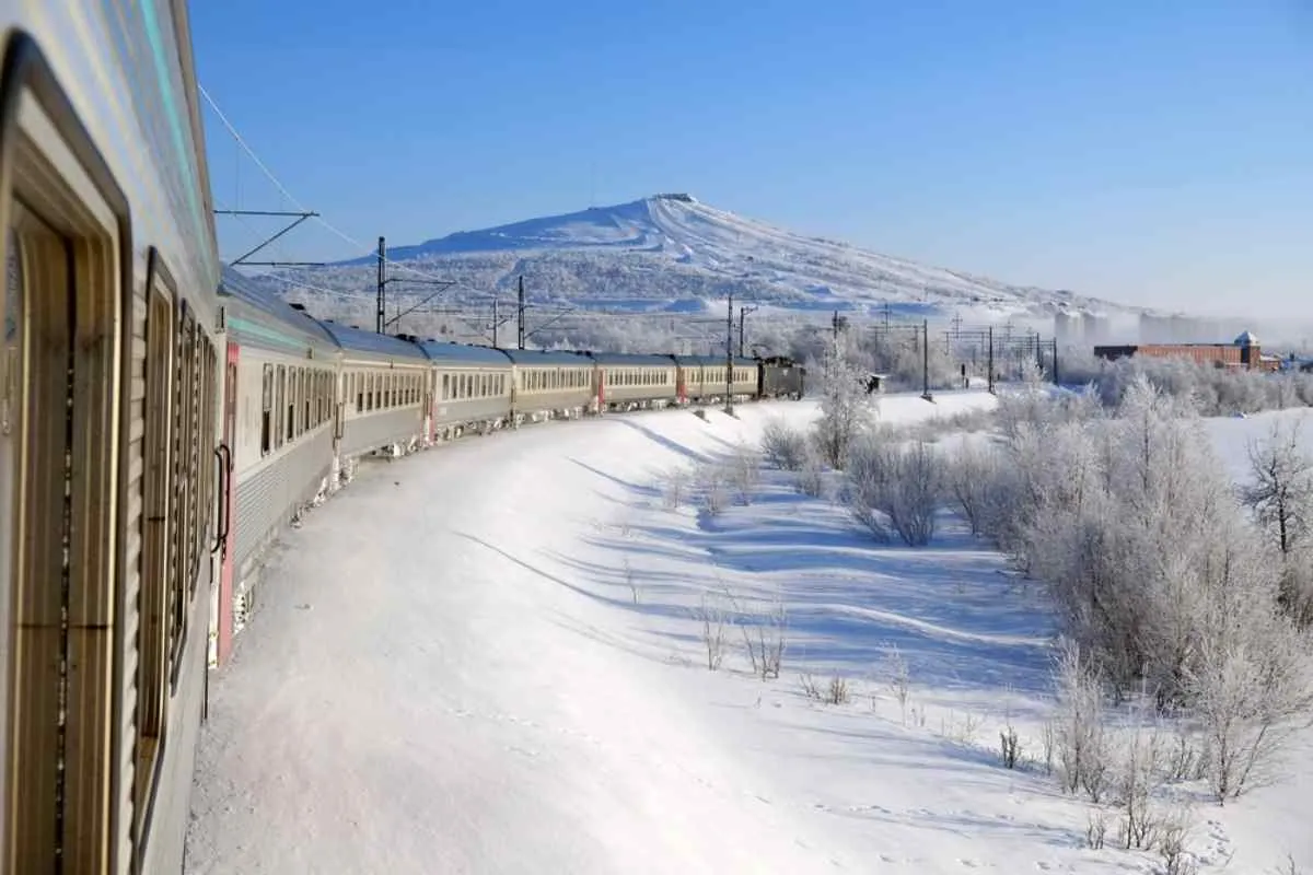 Vista generale di un treno in movimento che affronta una curva, ripreso frontalmente in un paesaggio innevato svedese.