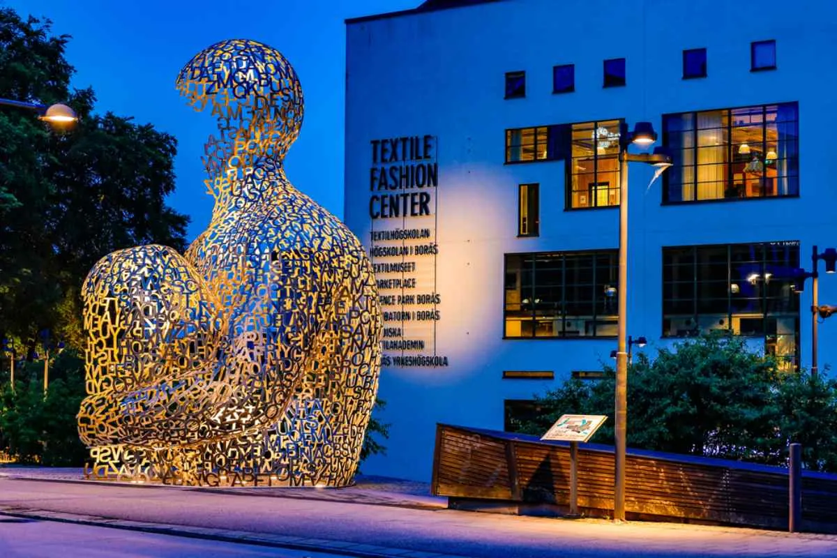 Sculpture représentant une silhouette humaine en forme de lettre, située à l'extérieur du Textile Fashion Center de Borås, à l'heure bleue.