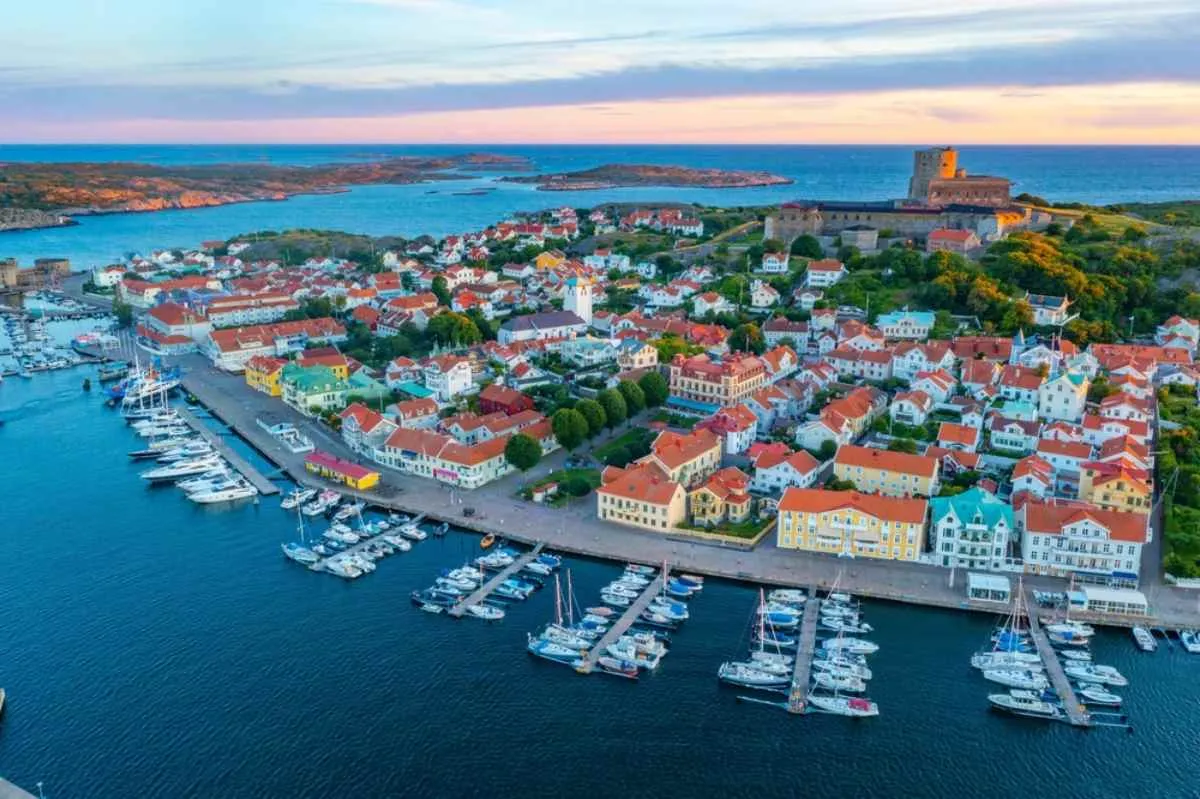 Une marina regorgeant de bateaux, des maisons colorées et la forteresse de Carlsten au coucher du soleil, sur la côte ouest de la Suède.