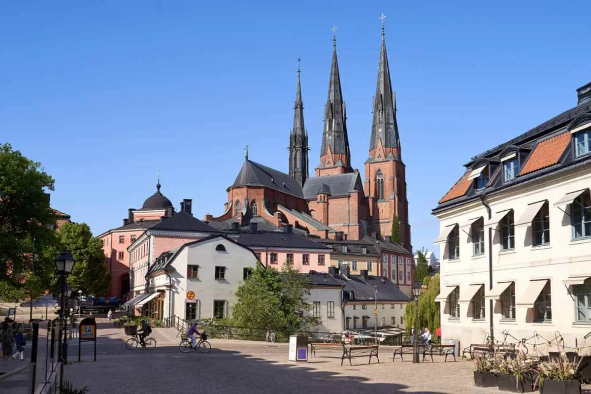 Les deux clochers de la cathédrale d’Uppsala surplombant une place pavée et des bâtiments aux couleurs pastel, par une journée ensoleillée.