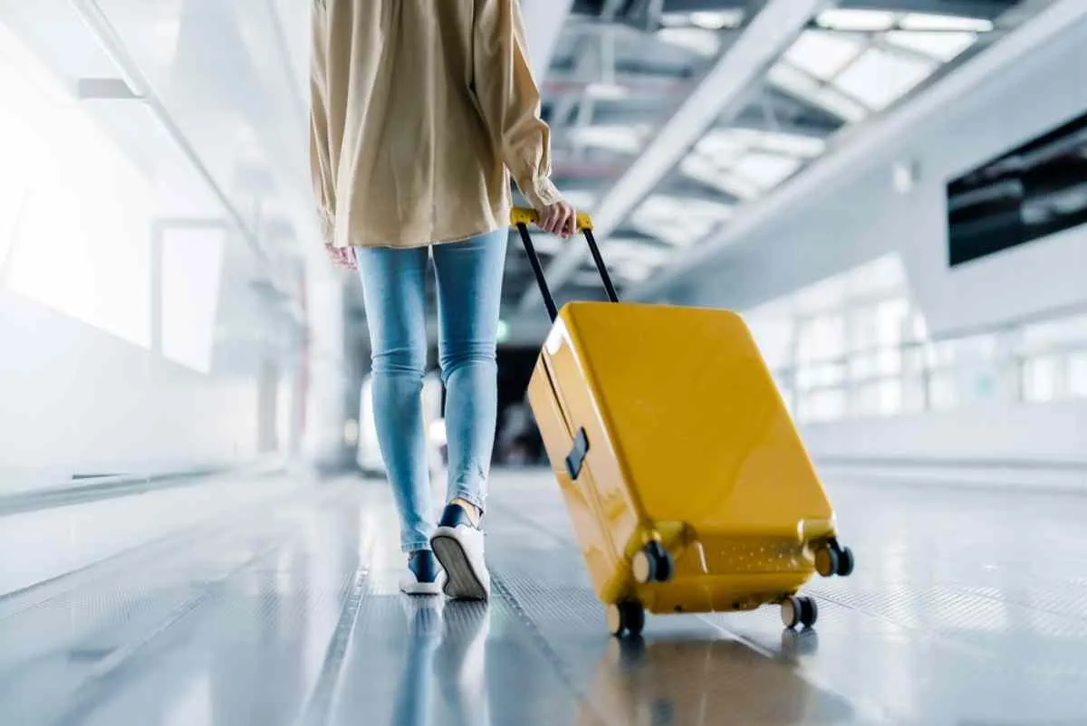Donna che cammina con una valigia gialla nel terminal di un aeroporto