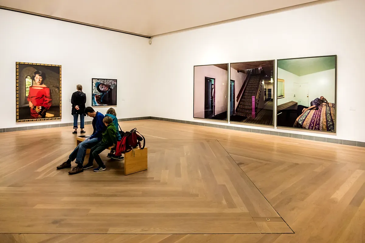 Des visiteurs au Moderna Museet, admirant des installations d’art contemporain dans une vaste salle d’exposition aux murs blancs minimalistes, au parquet et à l’éclairage tamisé.