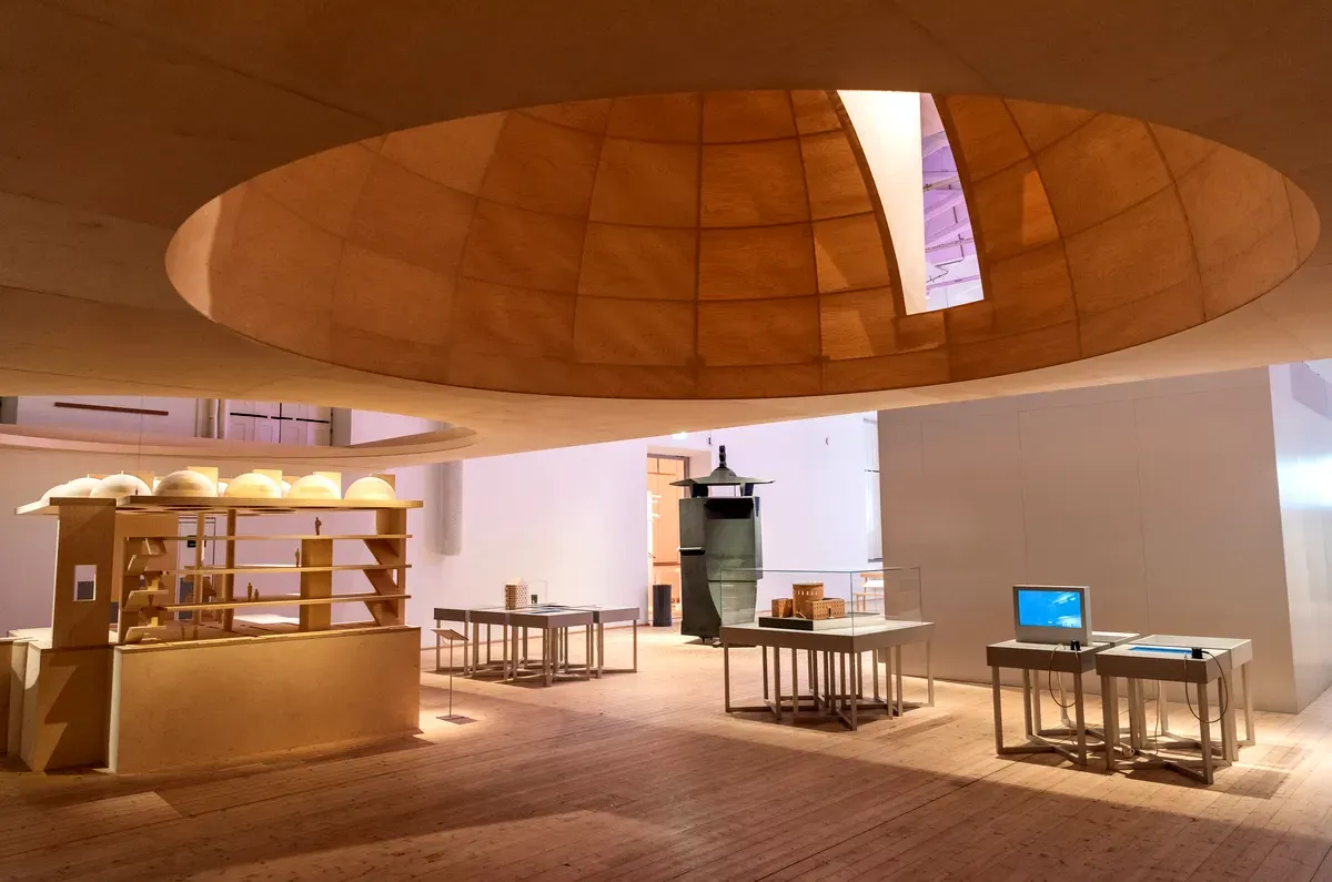 Vue intérieure du Moderna Museet à Stockholm, mettant en avant une structure architecturale en bois unique, avec des étagères, des tables et des œuvres d'art exposées sous une grande ouverture circulaire dans le plafond.