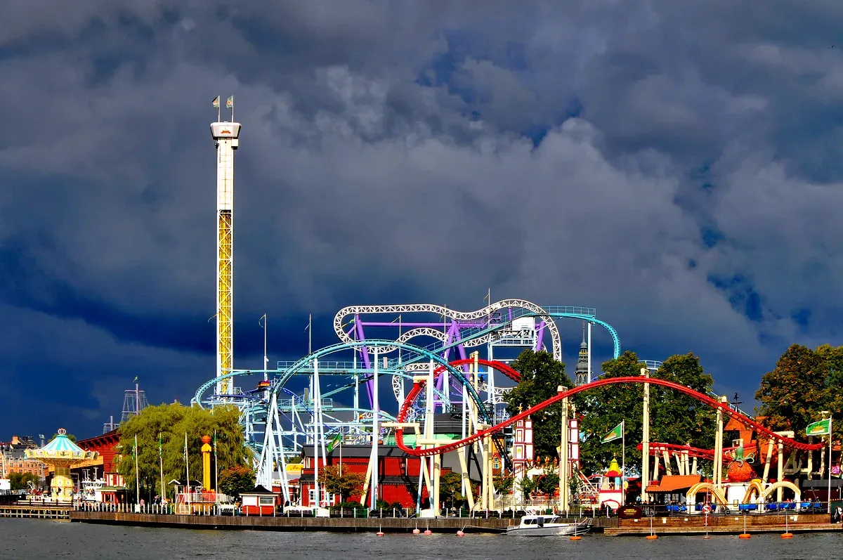 Una vista impresionante del parque de atracciones Gröna Lund en Estocolmo, en la que se ven varias montañas rusas de colores y atracciones altas bajo un cielo oscuro y espectacular.