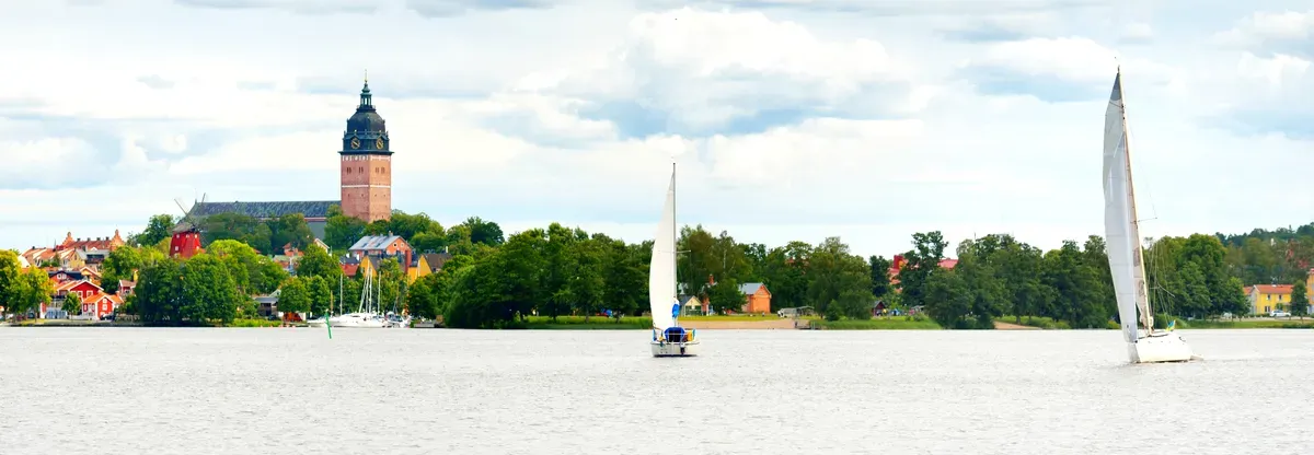 Vista panoramica delle barche a vela che scivolano sul lago Mälaren con la storica cattedrale di Västerås che si erge maestosa sullo sfondo, fondendo la bellezza naturale con il patrimonio culturale.