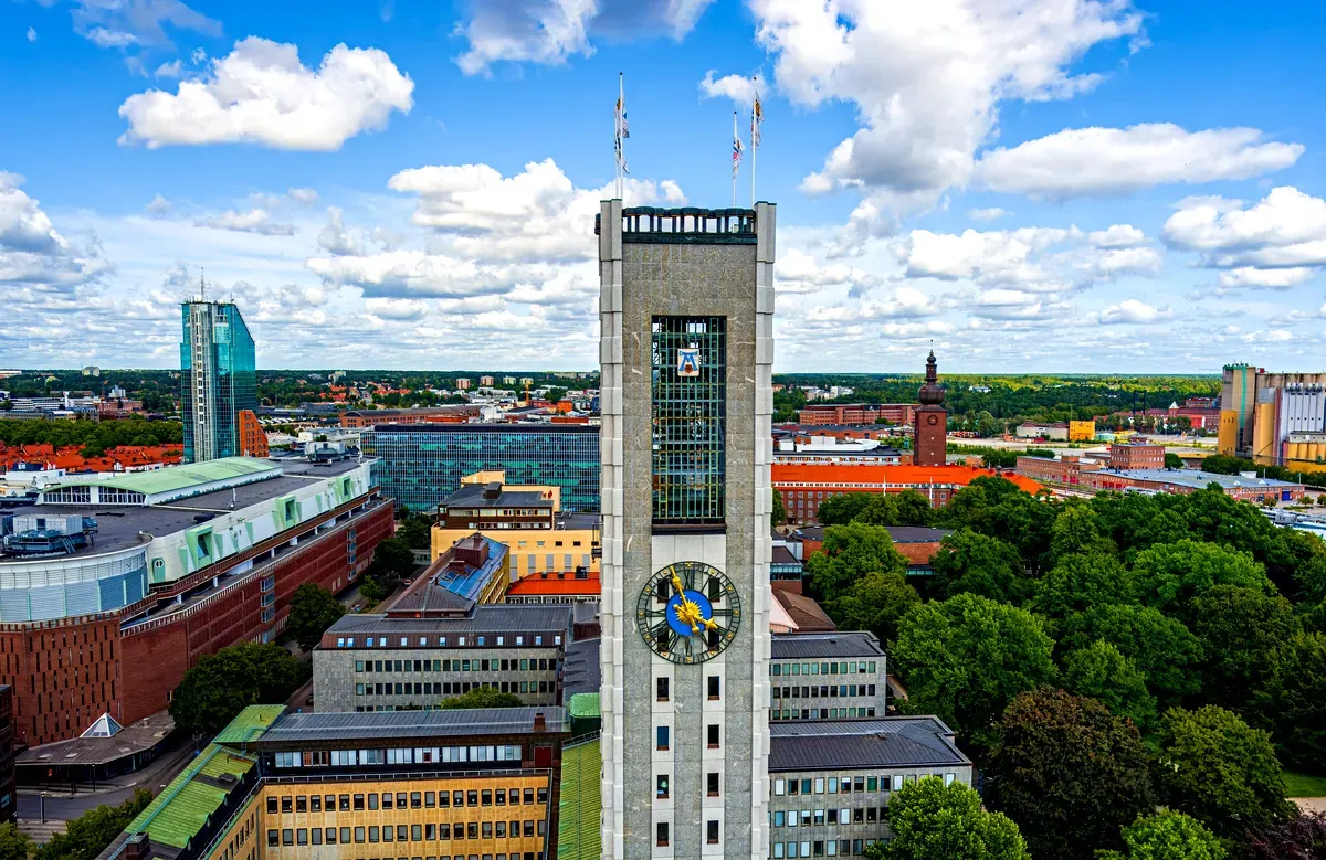 Una vista panoramica di Västerås, in Svezia, che mostra l’iconica torre dell’orologio della città, edifici moderni e storici e spazi verdi sotto un cielo azzurro e luminoso con nuvole sparse.