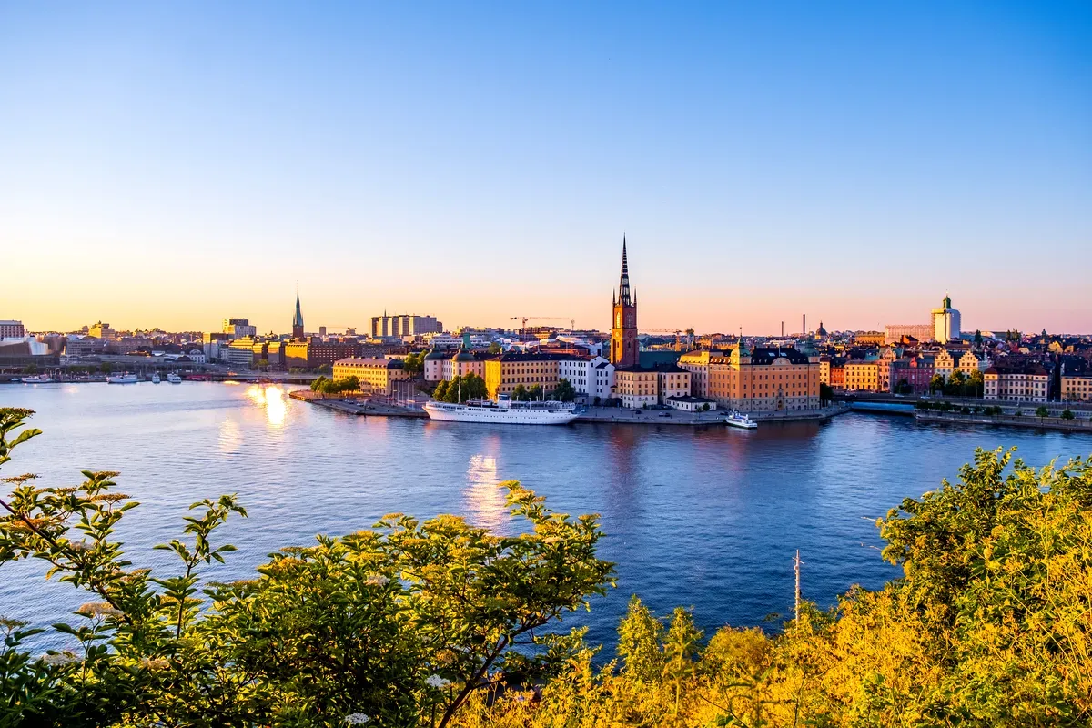 Impresionante vista panorámica del Gamla Stan de Estocolmo al atardecer, con edificios históricos, agujas y reflejos en el agua, vista desde Monteliusvagen