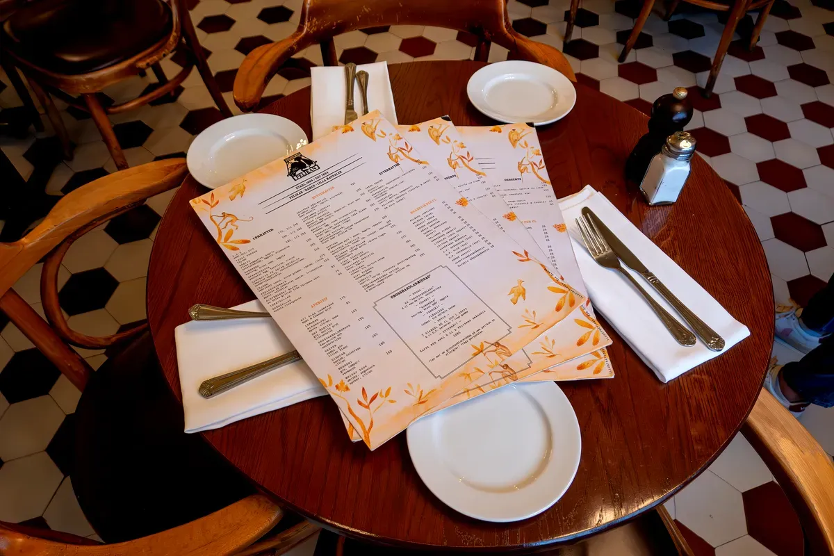Primer plano de una mesa de madera con menús, platos y cubiertos en el interior del histórico restaurante Pelikan de Estocolmo, que muestra su decoración tradicional.