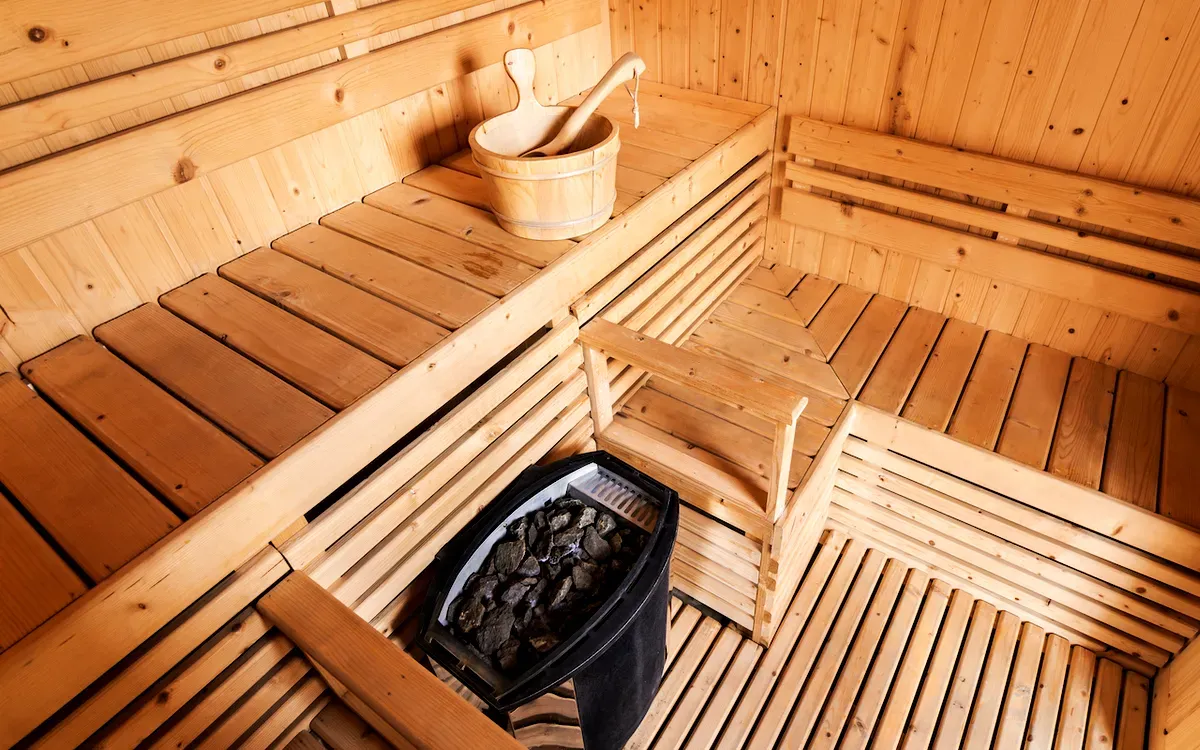 Intérieur traditionnel d’un sauna suédois en bois, avec un seau, une louche et un poêle, offrant une atmosphère chaleureuse et relaxante.