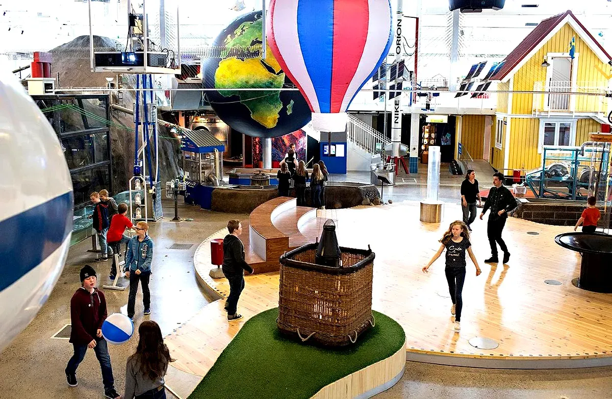 Niños explorando las exposiciones interactivas en Teknikens Hus, en Luleå (Suecia), donde destacan un globo aerostático y un globo terráqueo en un animado centro de ciencias.
