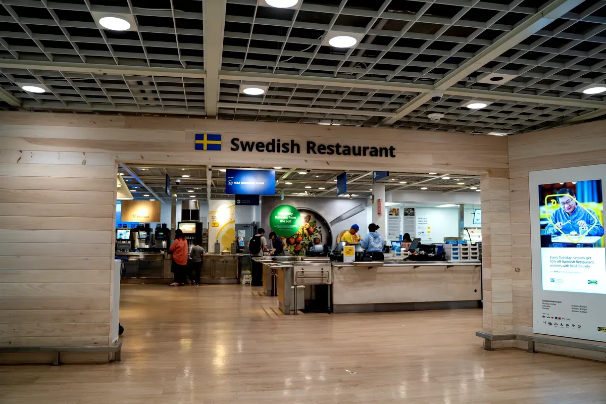 Entrée d’un restaurant suédois situé à l’intérieur d’un magasin IKEA, caractérisé par un design minimaliste et des tons de bois clairs. L’enseigne au-dessus de l’entrée indique 
