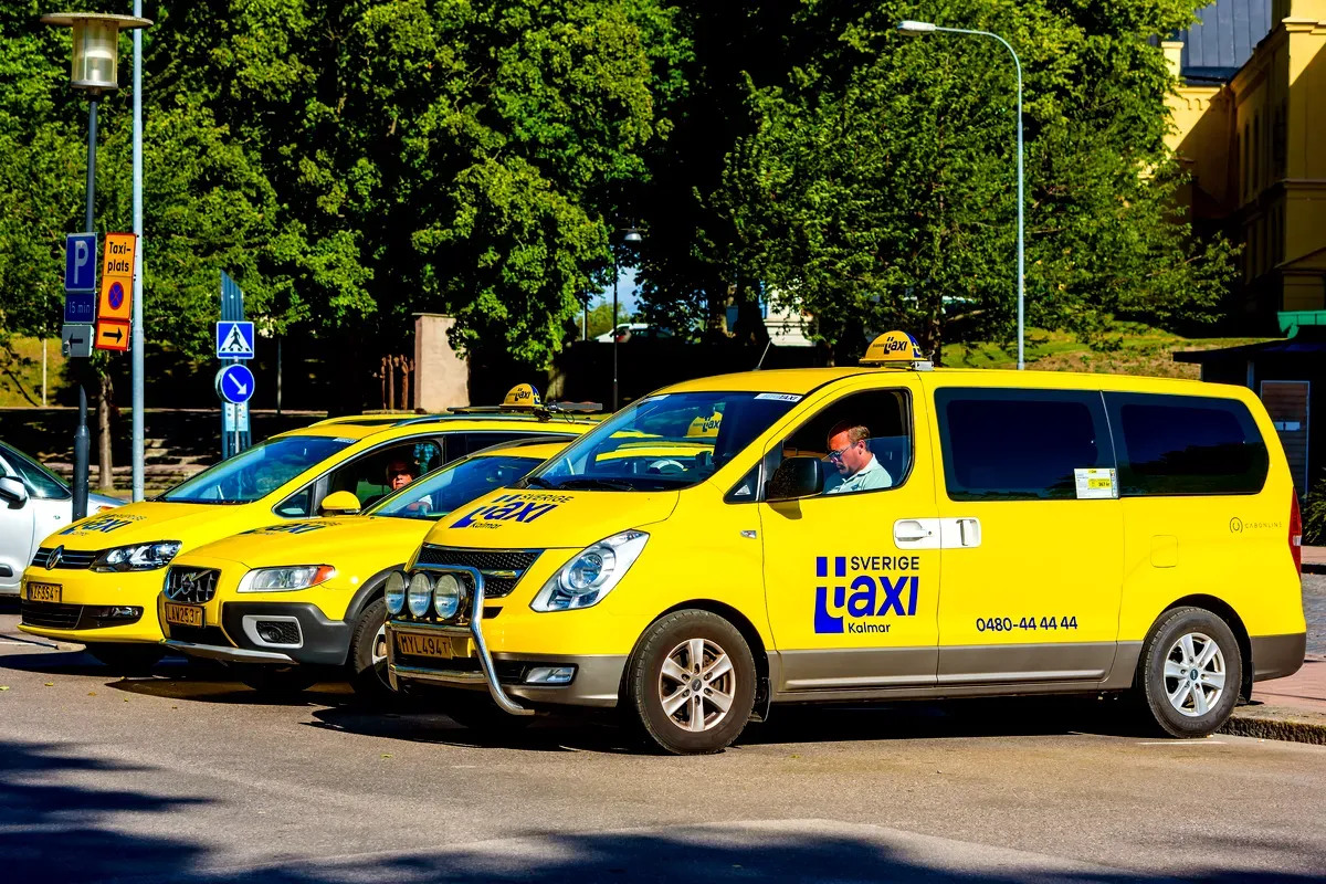 Des taxis suédois d'un jaune vif alignés à une station de taxis à Kalmar, en Suède, avec des chauffeurs attendant à l'ombre des arbres par une journée ensoleillée.