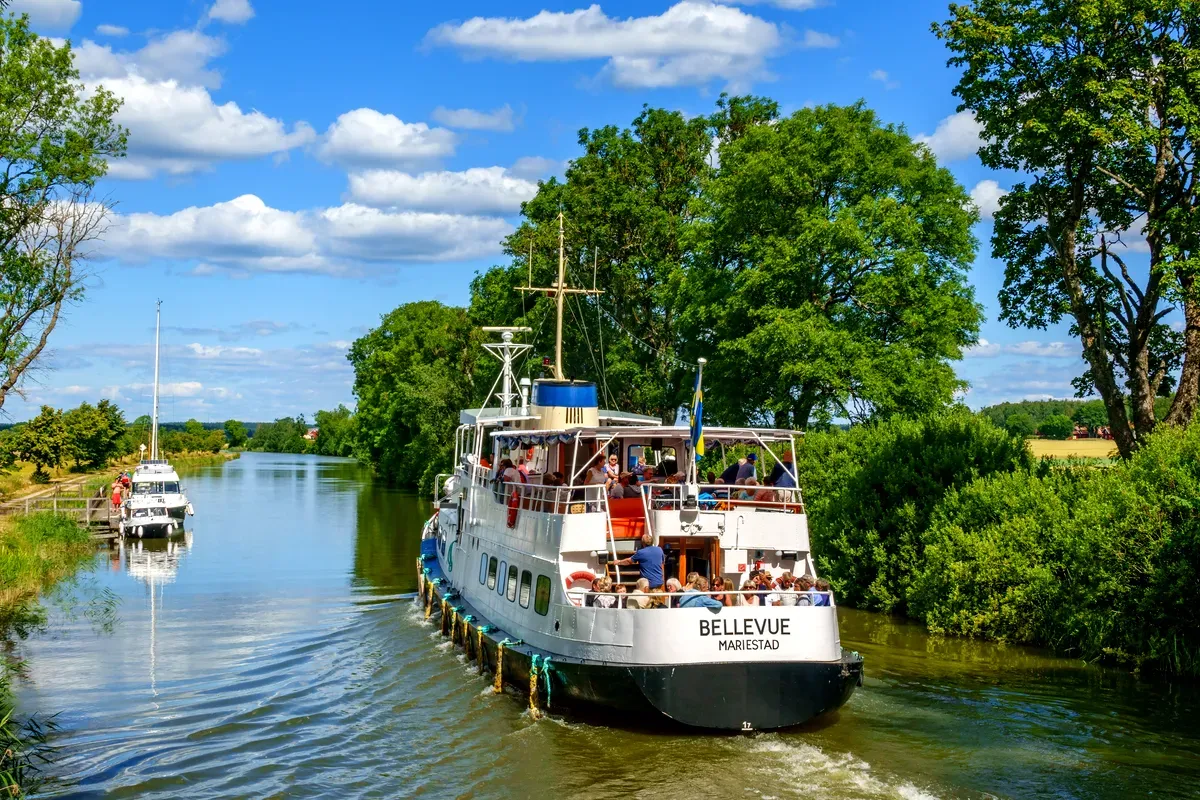 Il battello passeggeri Bellevue naviga lungo il pittoresco Canale di Göta a Mariestad, in Svezia, circondato da alberi rigogliosi e da un cielo azzurro e limpido.