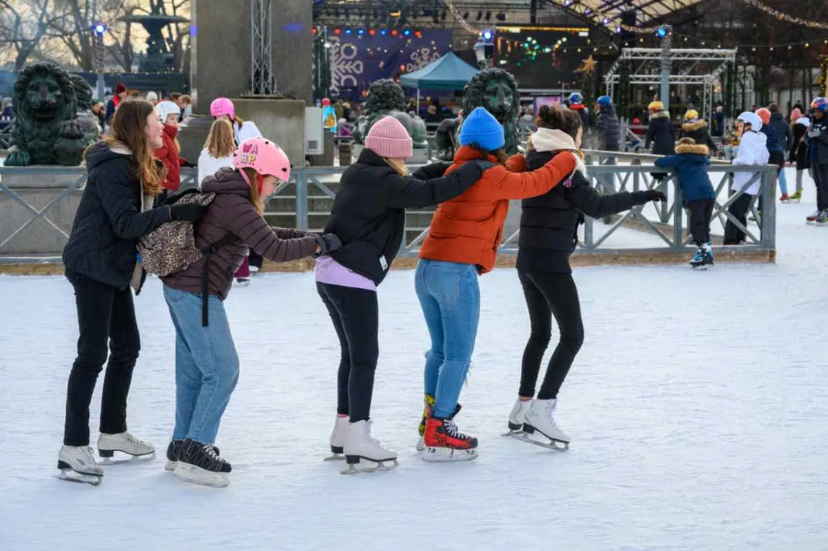 En grupp tjejer i Kungsträdgården, Stockholm, som står i rad och håller varandra i midjan medan de åker skridskor.