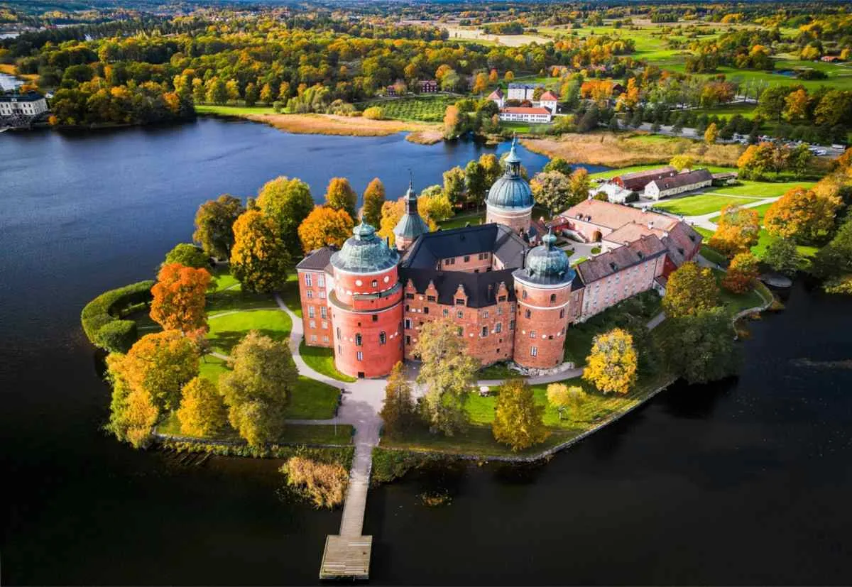 Drönarvy över Gripsholms slott i Sverige med dess karakteristiska rosa färg, runda fasad och den vackra sjön omkring.