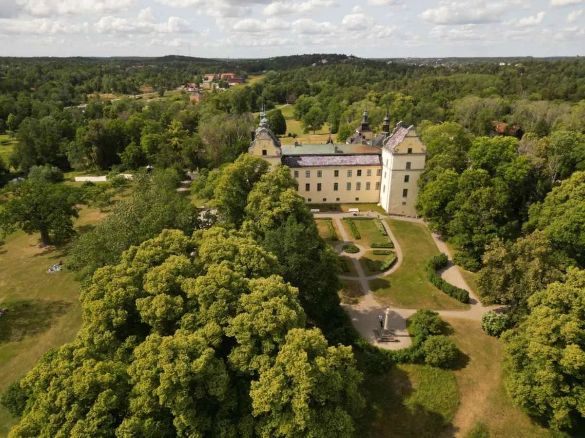 Drönarvy över Tyresö slott i Sverige med dess gula fasad och det stora grönområdet med trädgårdar och växtlighet.