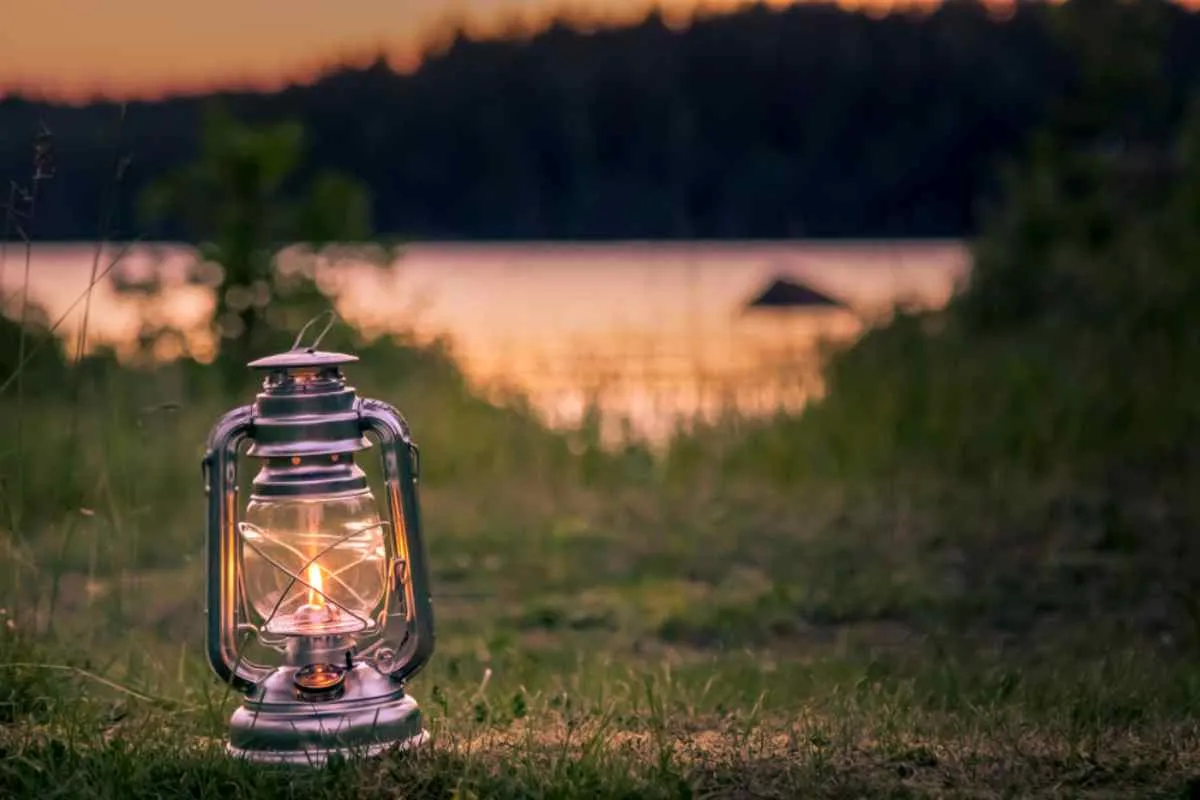 Una linterna vintage iluminando un camping con césped junto a un lago durante la puesta de sol en Suecia.