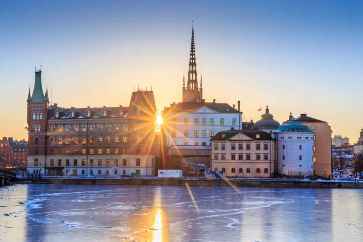 Puesta de sol detrás de los edificios históricos de Riddarholmen, en Estocolmo (Suecia), con agua helada en primer plano.