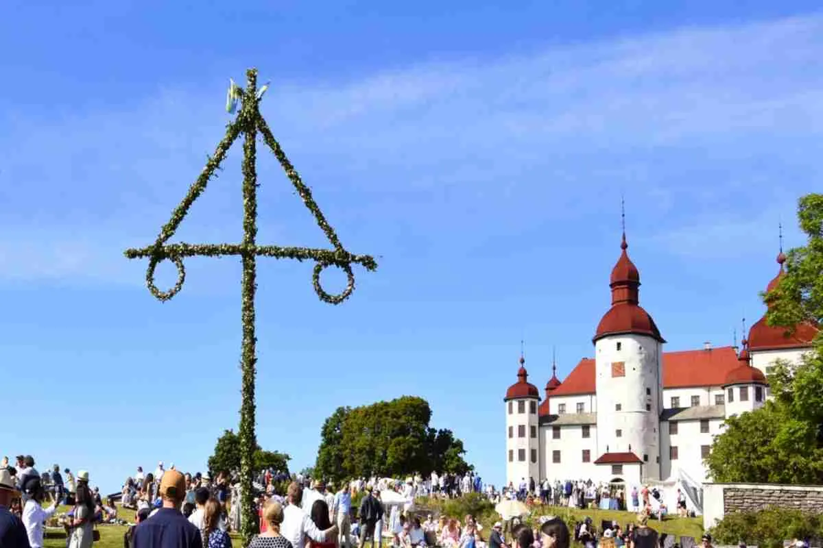 Croix typiquement suédoise composée de fleurs et érigée au milieu d’une prairie verdoyante, où une foule s’est rassemblée pour célébrer la fête de la Saint-Jean.
