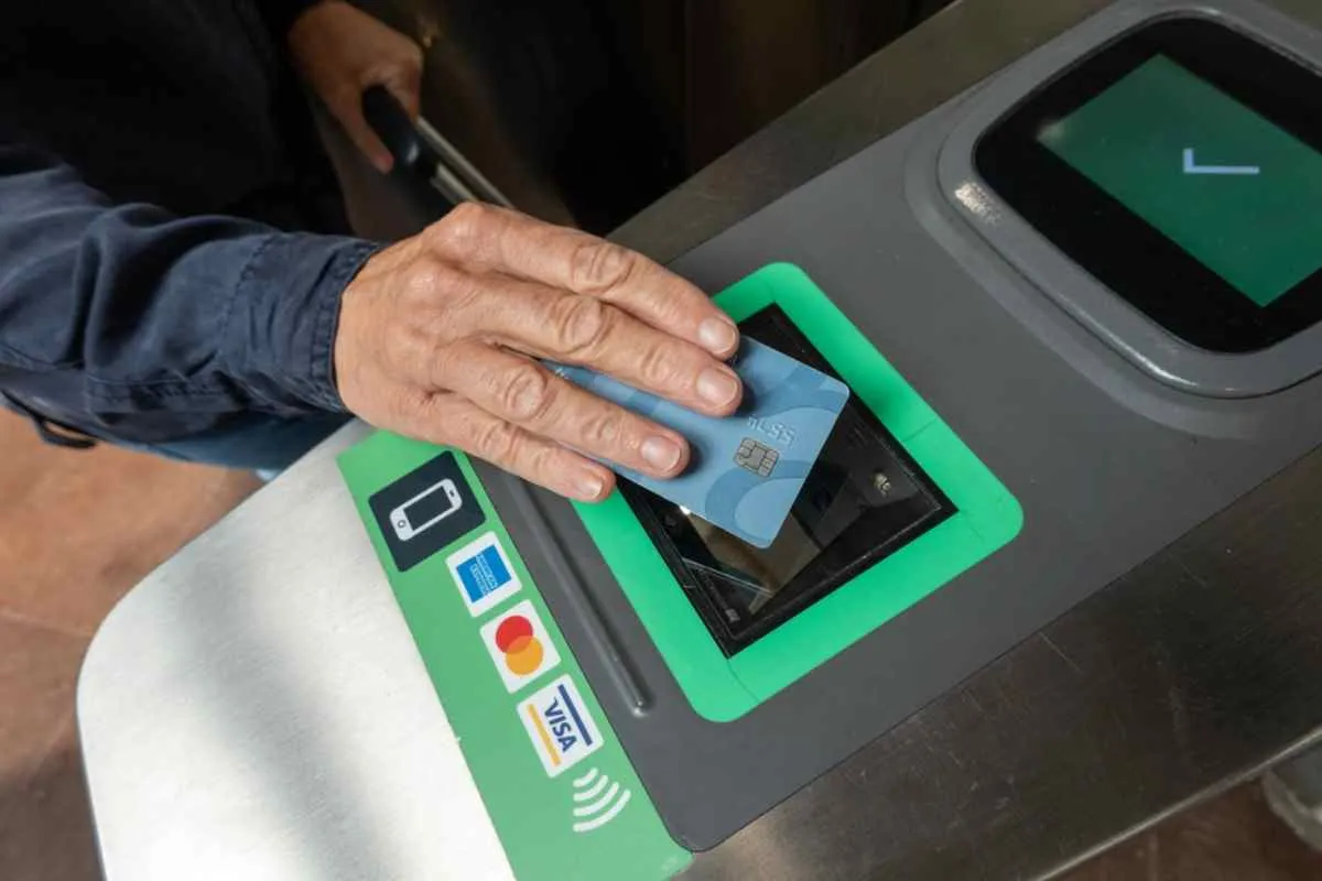 Un homme passe sa carte bancaire devant un lecteur qui semble se trouver dans une station de transports en commun et qui accepte plusieurs réseaux.