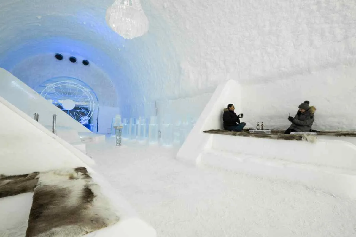 Una pareja de turistas, vestidos con ropa de abrigo, están sentados sobre un bloque de hielo dentro del famoso hotel de hielo de Suecia.