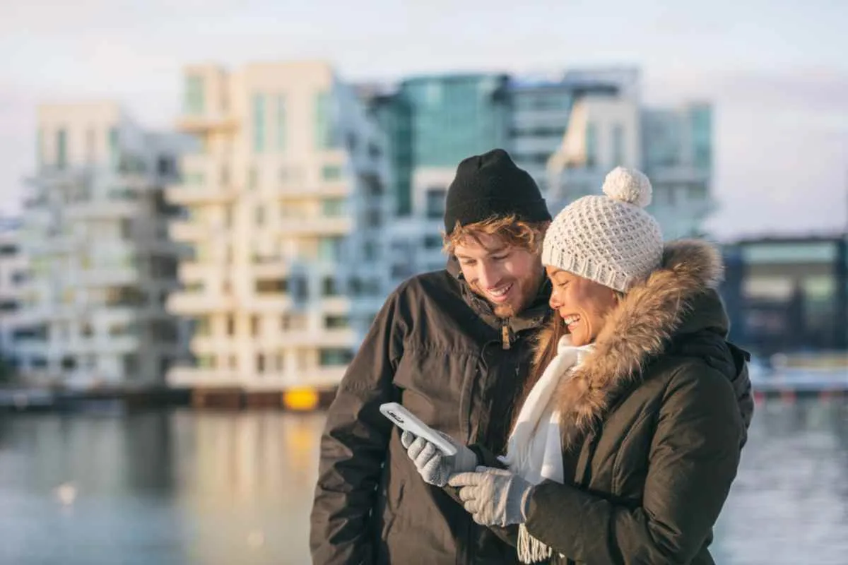 Un couple souriant, vêtu de vêtements chauds, regarde l'écran du téléphone portable que tient la jeune femme.