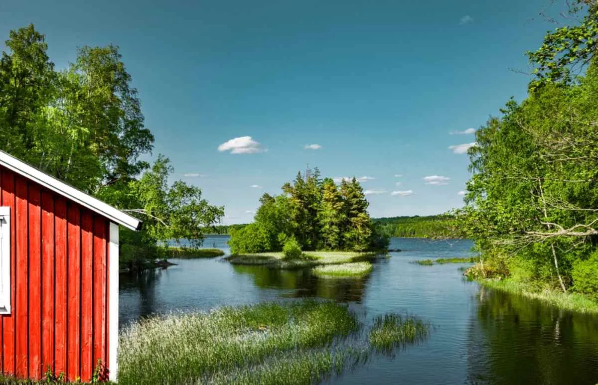 Un lago rodeado de árboles se extiende junto a lo que parece ser una cabaña de camping en Suecia, en un día soleado.