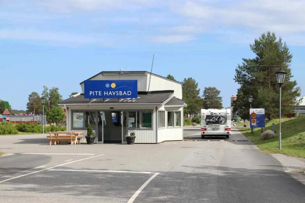 Vue d'ensemble de la guérite du camping Pite Havsbad en Suède, avec un camping-car transportant des vélos à l'arrière qui franchit le portail d'entrée.