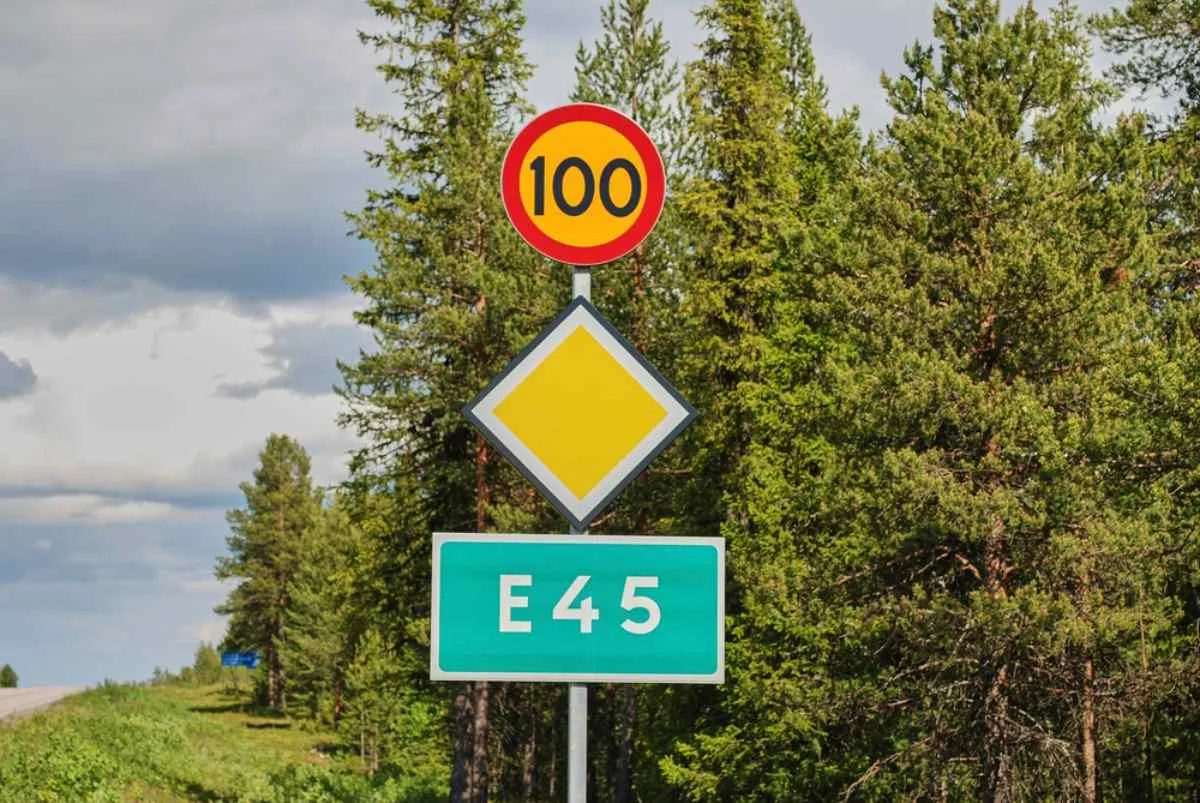 Panneau de l'autoroute E45 et signal de priorité dans une forêt de pins.