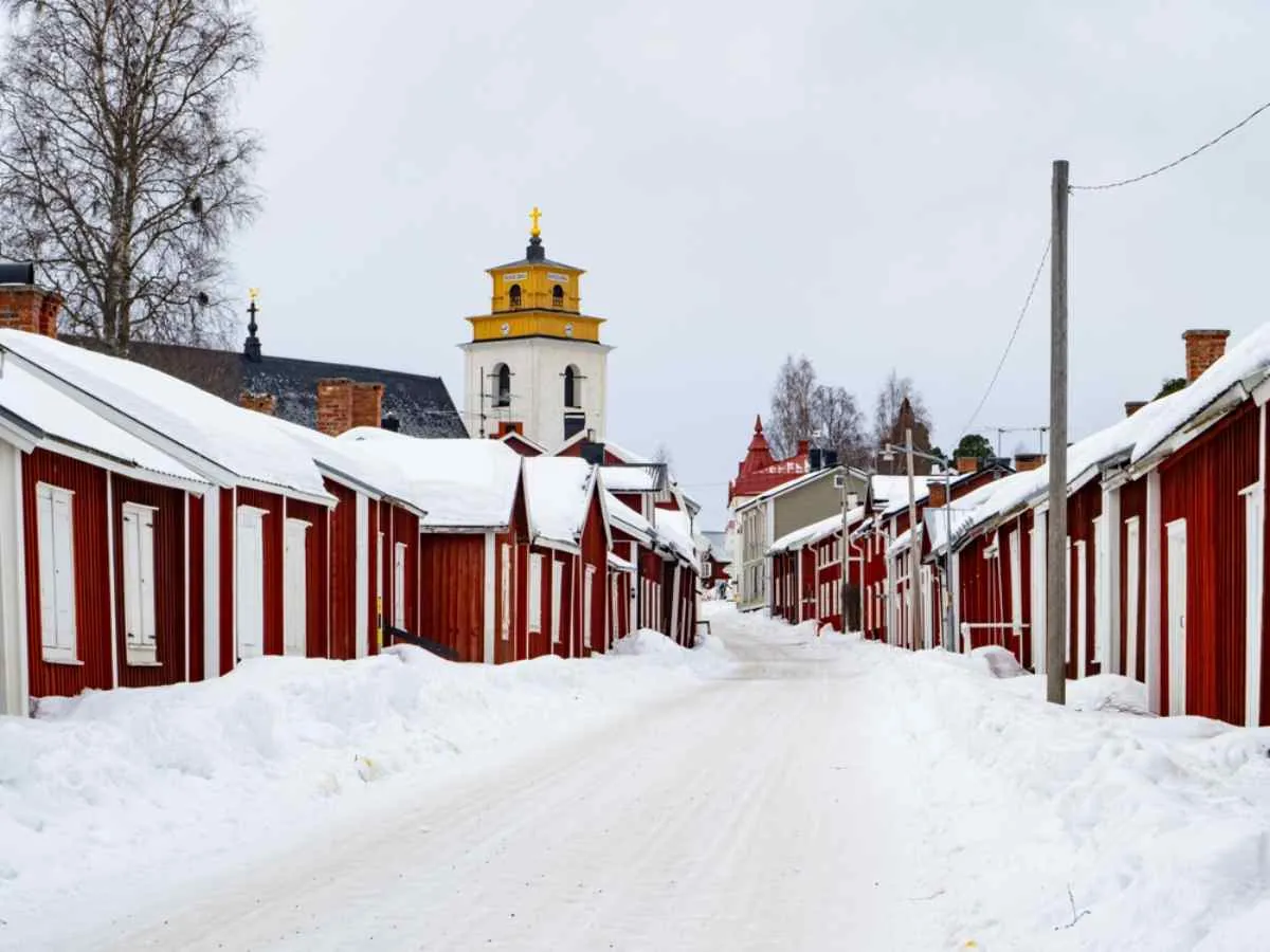Rue enneigée bordée de maisons en bois rouges dans la ville-église de Gammelstad.