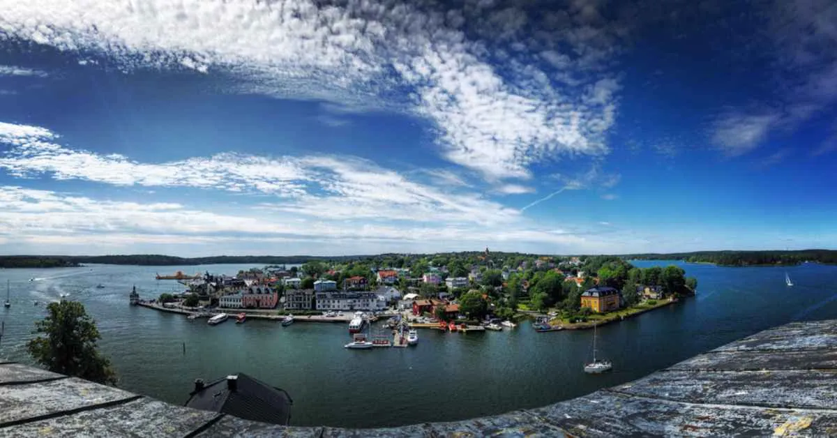 Vue panoramique sur le port de Vaxholm et l’archipel de Stockholm, avec des bateaux, des maisons colorées et un ciel radieux lors d’une excursion estivale d’une journée.