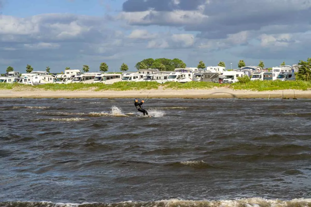 Un kitesurfeur surfant sur des vagues agitées devant une longue rangée de camping-cars dans un camping en bord de mer sur la côte ouest de la Suède, l’endroit idéal pour les campeurs actifs.