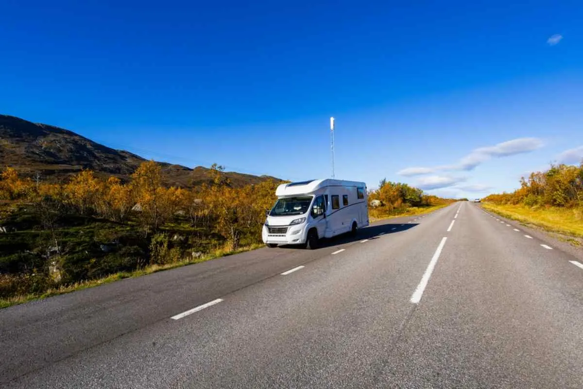 Una autocaravana blanca circulando por una carretera asfaltada desierta a través de la tundra abierta y los colores otoñales, bajo un cielo azul brillante en el norte de Suecia.
