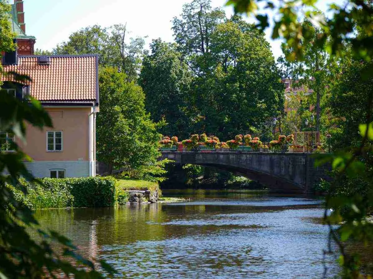 Un ponte fiancheggiato da fiori sul fiume Nyköping, con case storiche e una vegetazione rigogliosa: una bella tappa durante un viaggio on the road da Stoccolma.