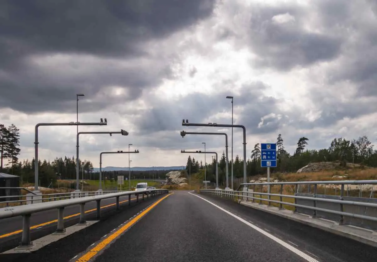 Autopista noruega con pórticos de peaje AutoPASS bajo un cielo nublado, vista desde la perspectiva del conductor.