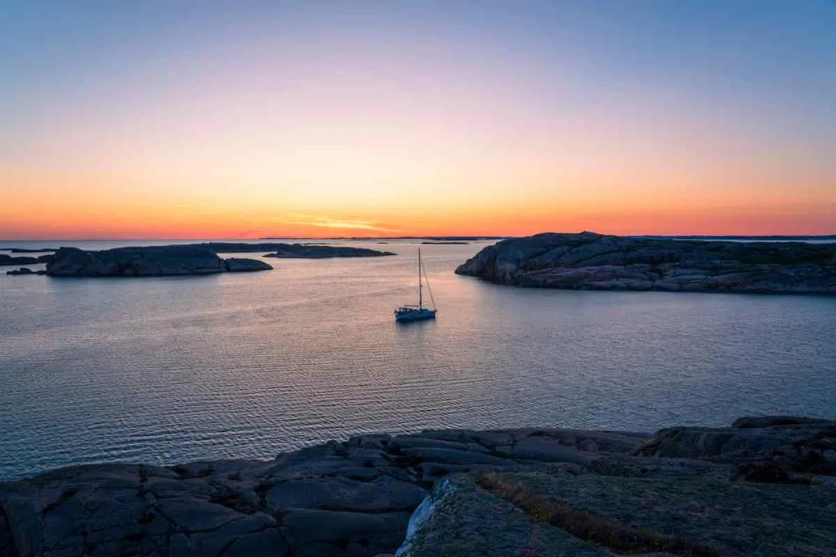 La costa rocosa de Bohuslän al atardecer, con un pequeño velero anclado entre islotes de granito liso.