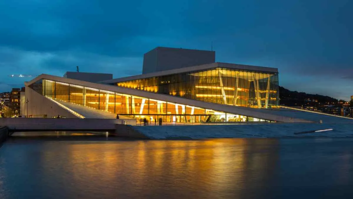 La Ópera de Oslo iluminada al atardecer, con su arquitectura moderna reflejada en las tranquilas aguas del puerto.
