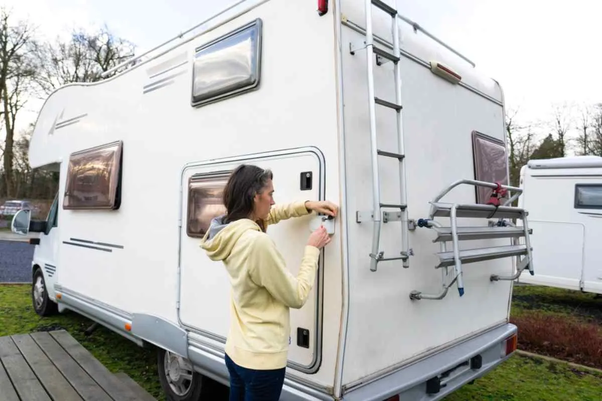Une femme vérifie la trappe extérieure d’un camping-car dans un camping, avec un autre camping-car à proximité.